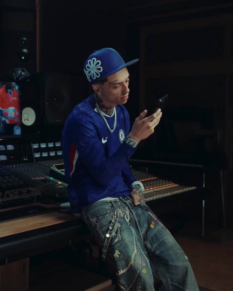 A person wearing a Chelsea football jersey uses a smartphone in a recording studio.