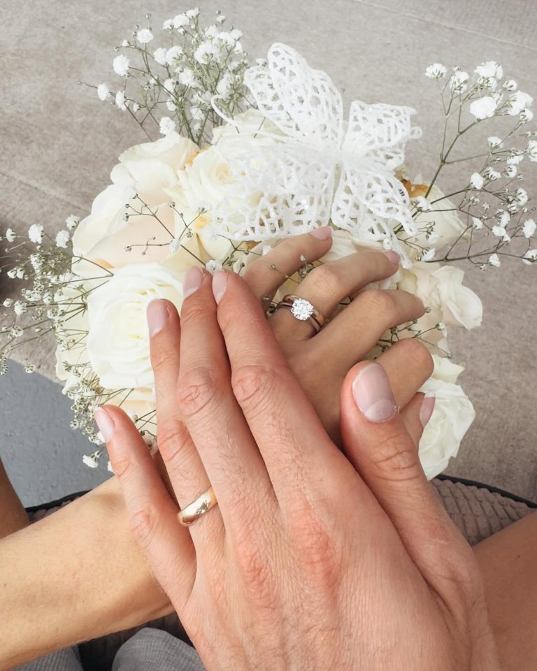 Couple's hands with wedding rings on a bouquet of white roses.
