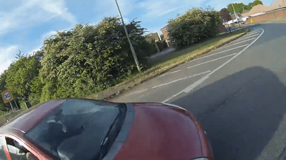 Screenshot of a red car driving on a residential road.