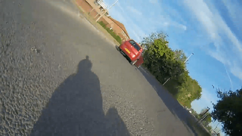 Screenshot of a red car driving away from the camera on a residential street.