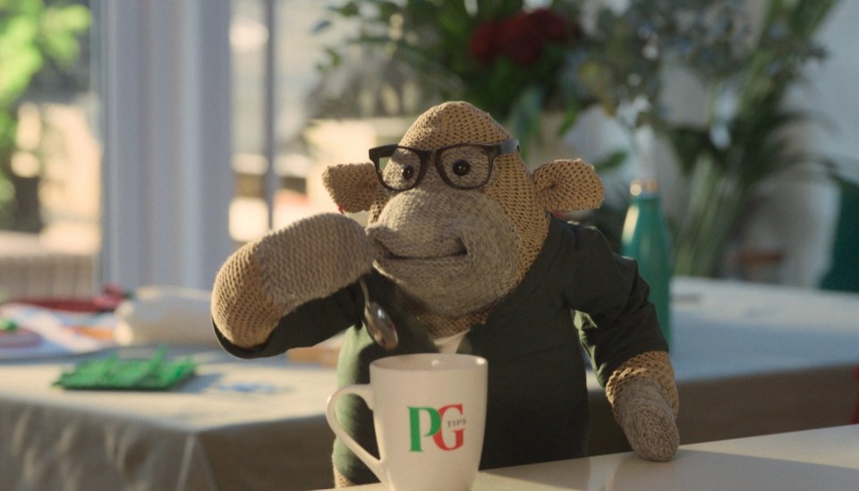 A knitted monkey wearing glasses stirs a cup of PG Tips tea.