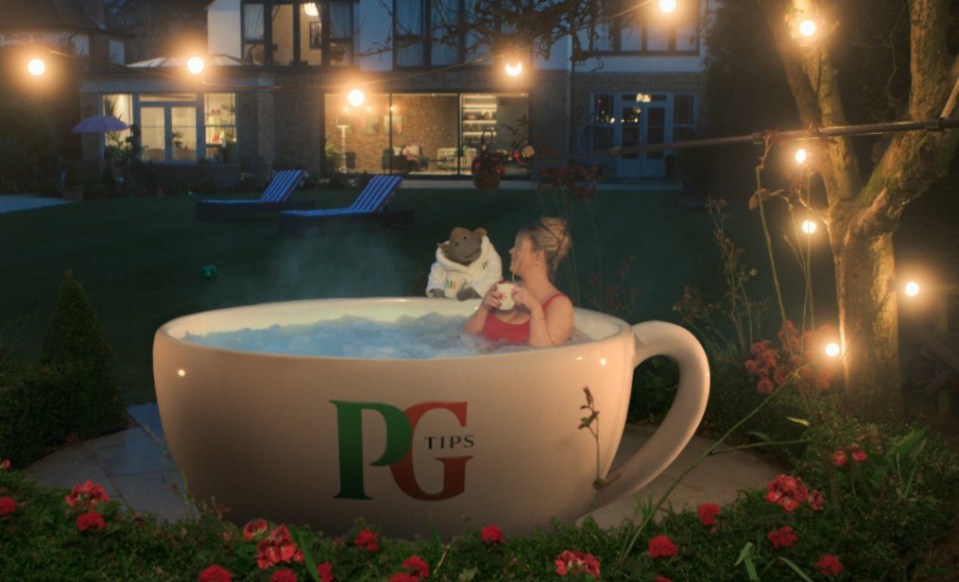 Woman and monkey relaxing in a giant teacup hot tub at night.