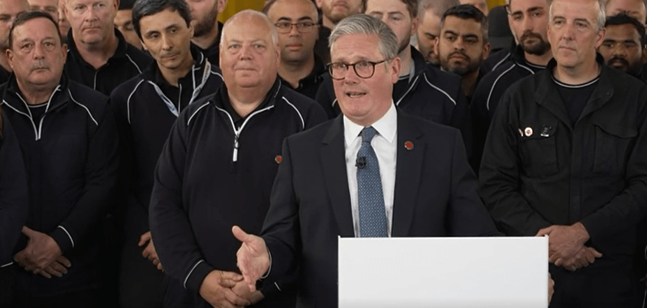 Man in suit speaking to a group of men in uniform.