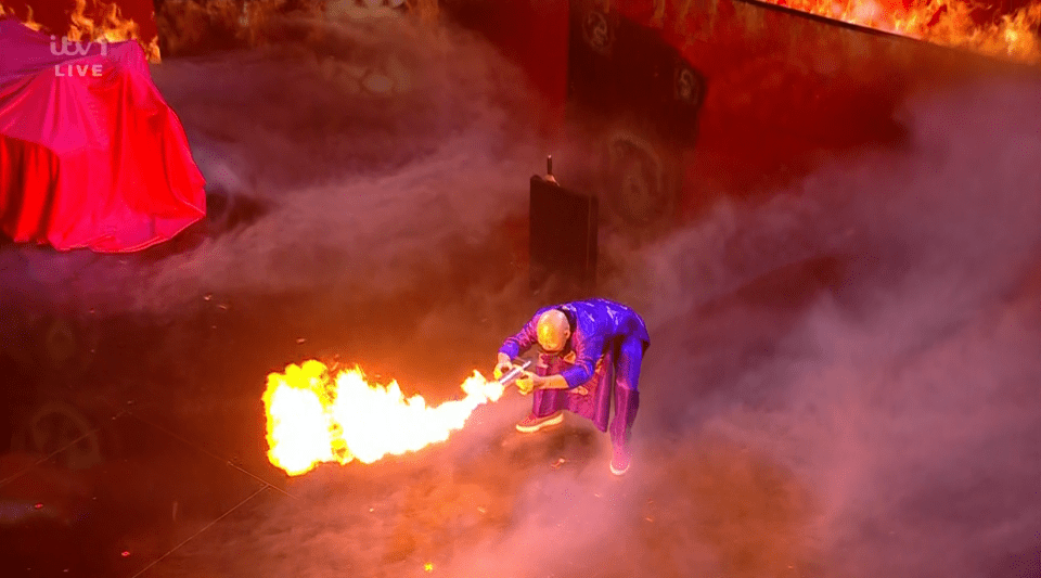A performer breathes fire on a stage.