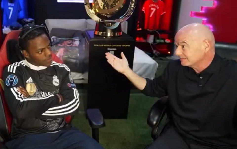 Screenshot of two men seated, one in a Real Madrid jersey, the other in a black polo shirt, conversing near a FIFA Club World Cup trophy.