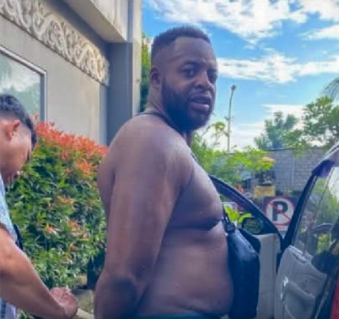 Shirtless man with a dark-colored bag across his shoulder.