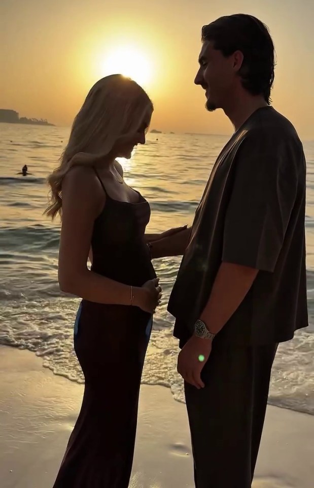 Silhouette of pregnant woman and man on beach at sunset.