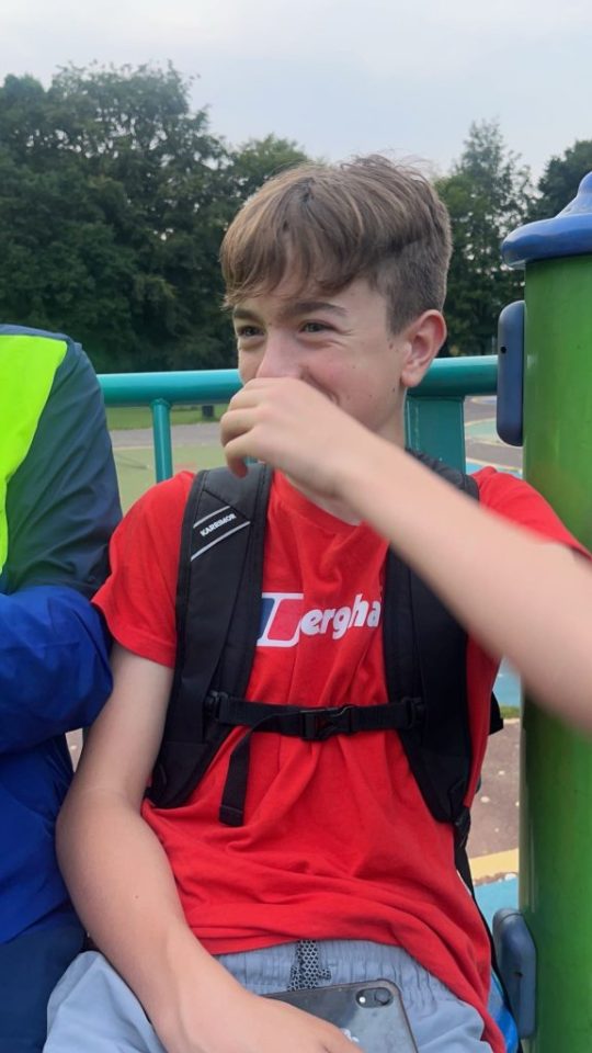 Teenage boy laughing, wearing a red shirt and backpack.