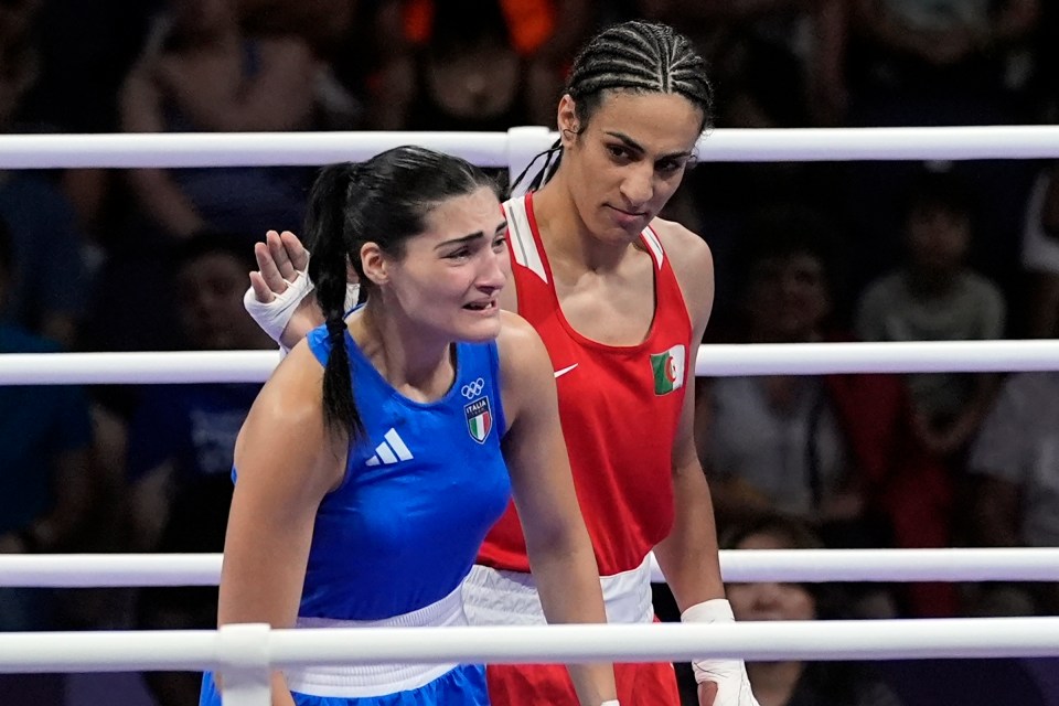 A tearful Italian boxer in a blue uniform stands next to an Algerian boxer in a red uniform after a boxing match.