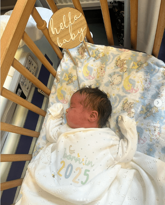 Newborn baby sleeping in a crib with a "Hello Baby" sign.