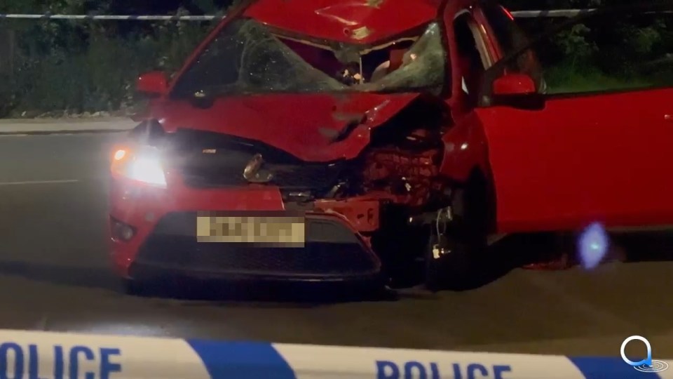 Damaged red car at a crime scene.
