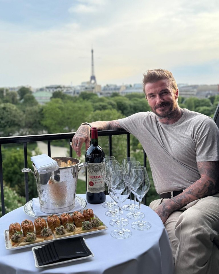 David Beckham on a balcony in Paris with wine and appetizers, the Eiffel Tower in the background.