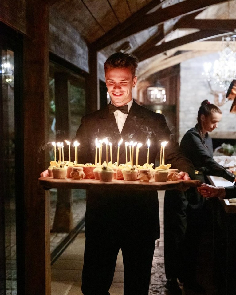 A waiter carries a tray of cupcakes with lit candles.