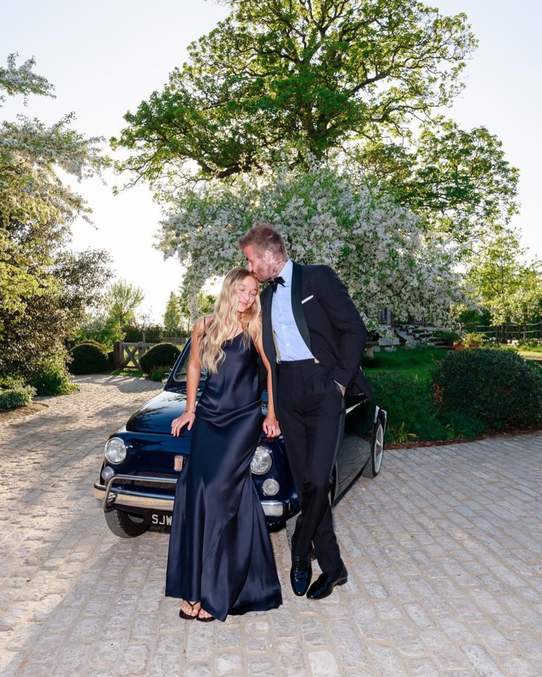 David Beckham kissing his daughter Harper Seven on the forehead, while standing next to a classic car.