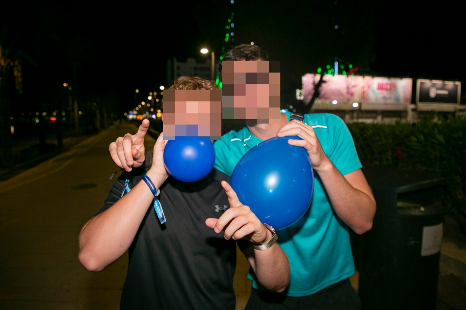 Two people inflating blue balloons at night.