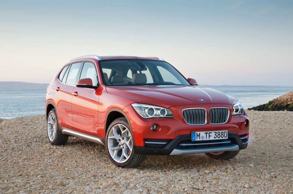 Red BMW X1 sDrive 20d parked on a rocky beach.