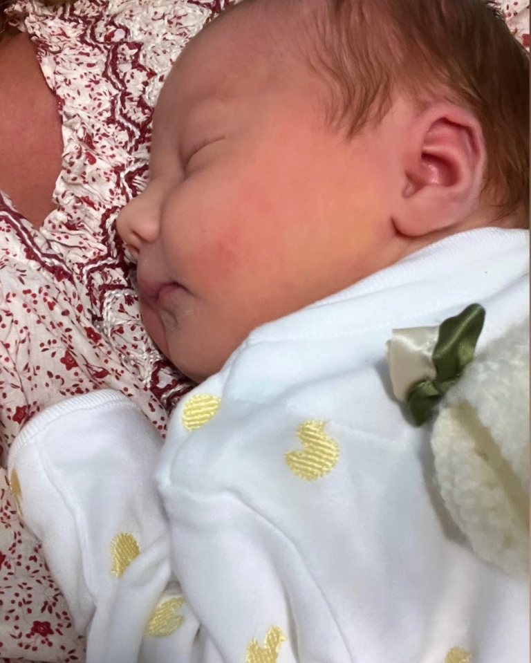 Sleeping newborn baby wearing a white onesie.