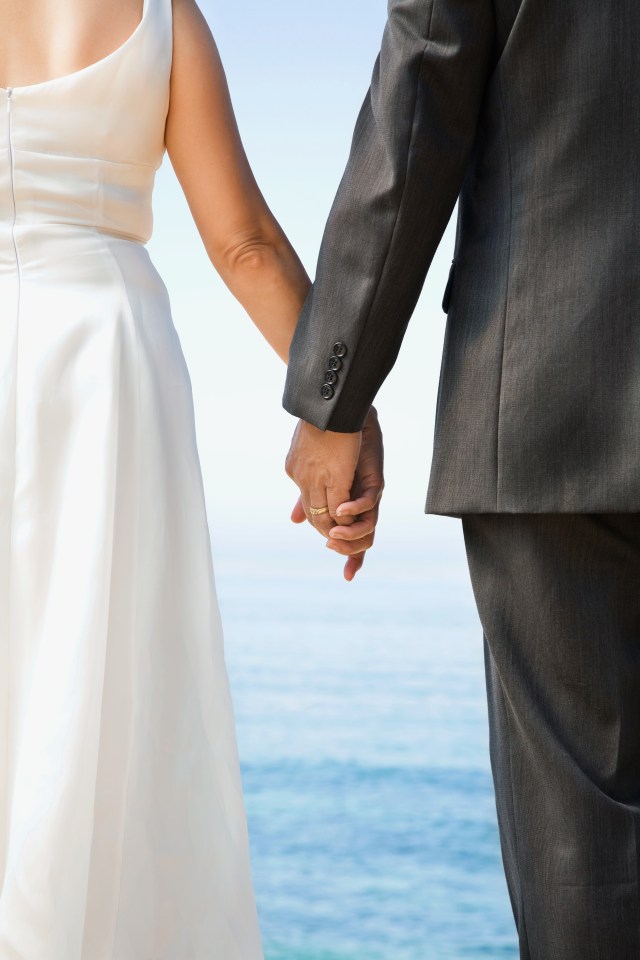 Bride and groom holding hands by the ocean.