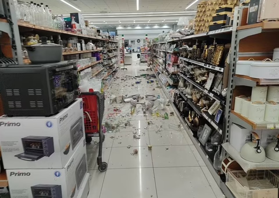Store aisle with shattered glass and fallen merchandise after an earthquake.