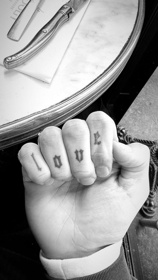 Black and white photo of a hand with "LOVE" tattooed on the fingers.