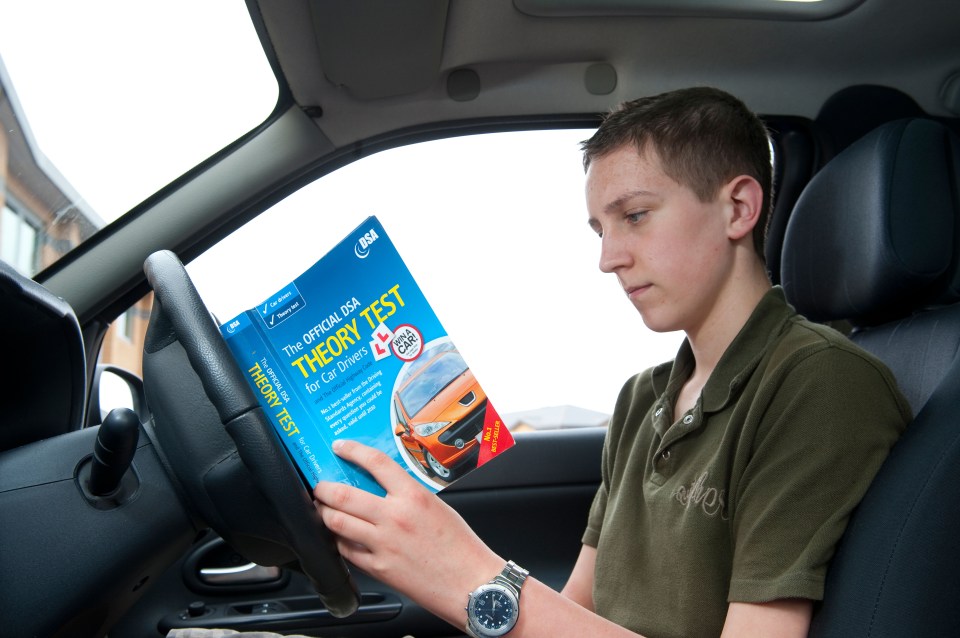 Teenage boy studying driving theory test handbook in car.