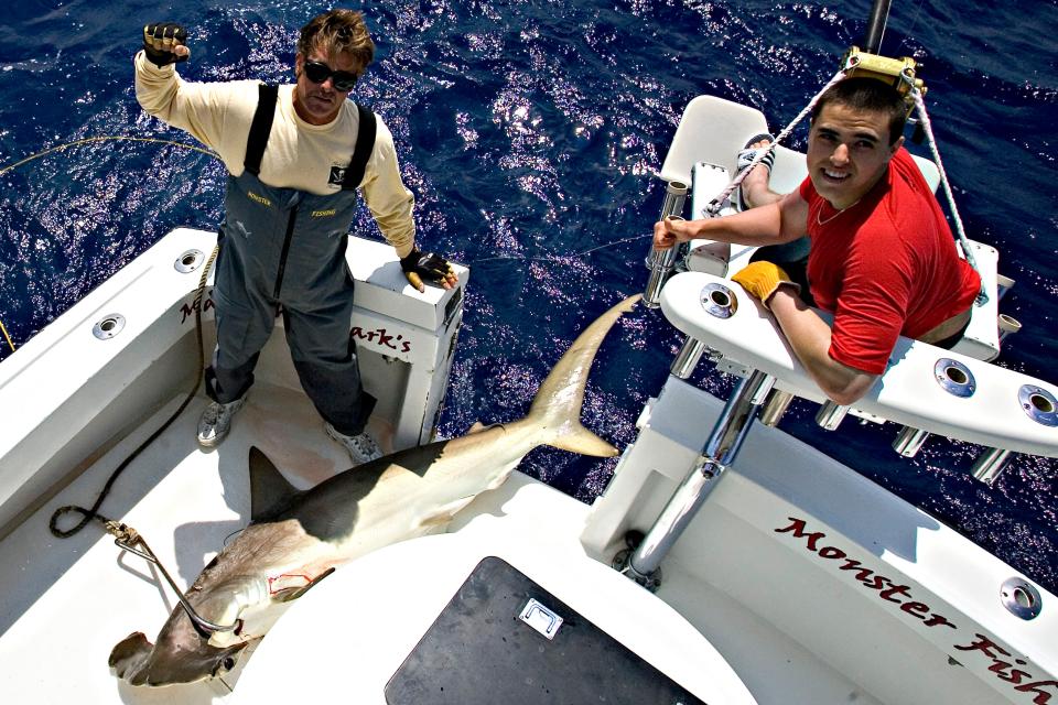 Two men on a boat holding a large hammerhead shark.