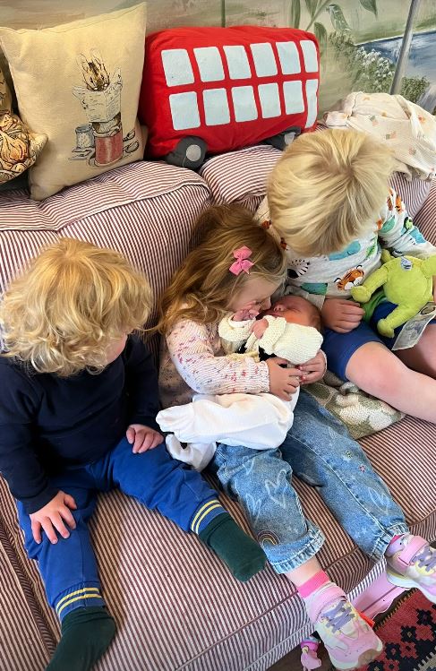 Three young children cuddling a baby on a couch.