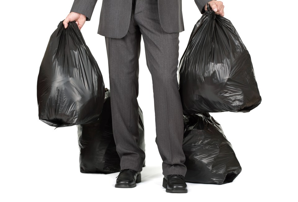 Man in suit carrying multiple black garbage bags.