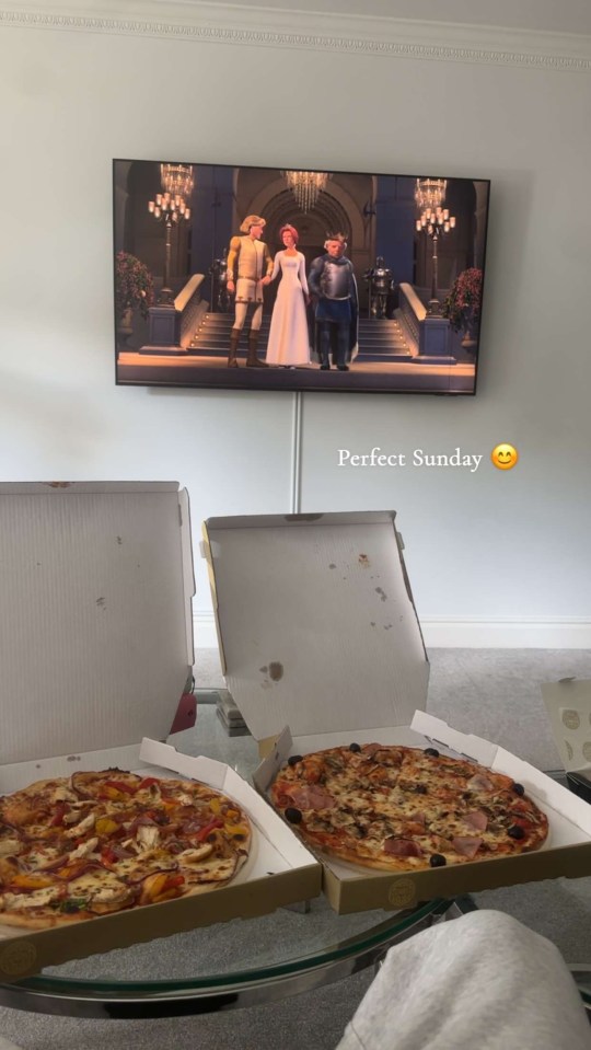 Two pizzas and a TV showing a movie.