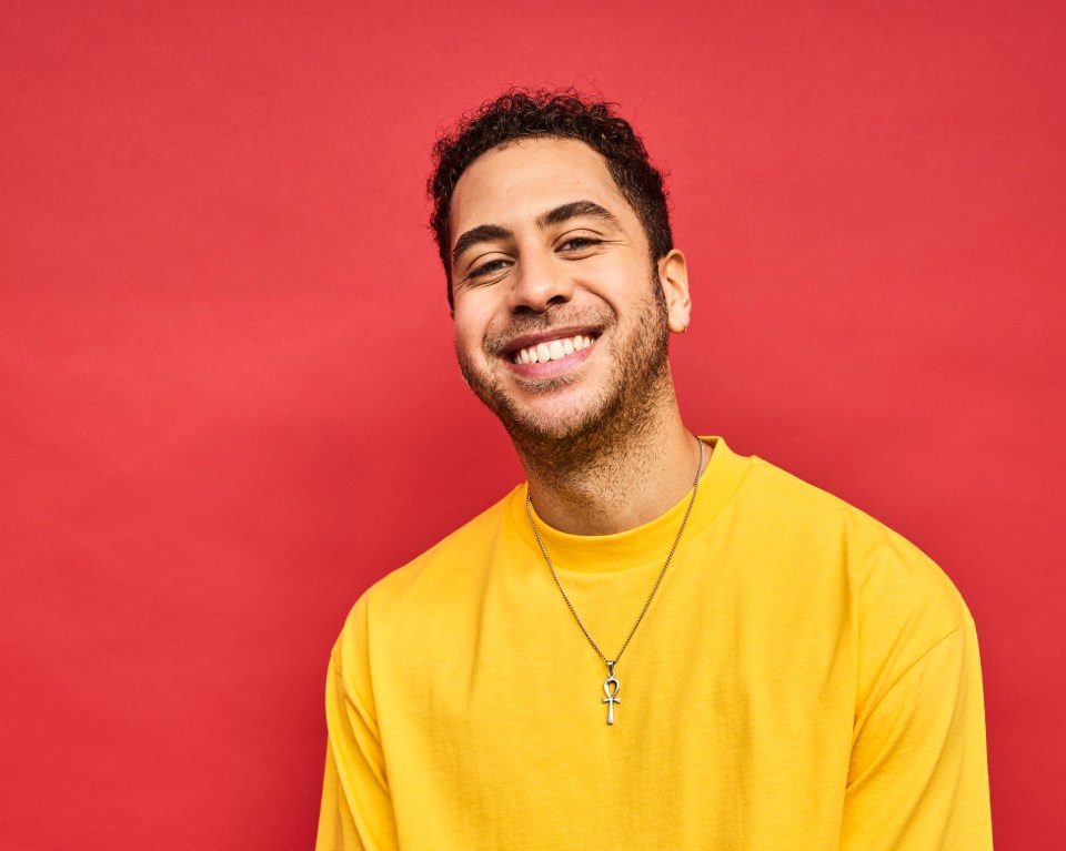 Portrait of a smiling young man wearing a yellow shirt and an ankh necklace.