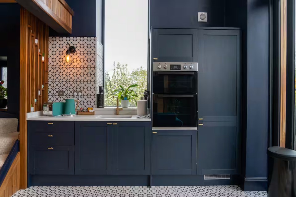 Dark blue kitchen with double oven and patterned tile backsplash.