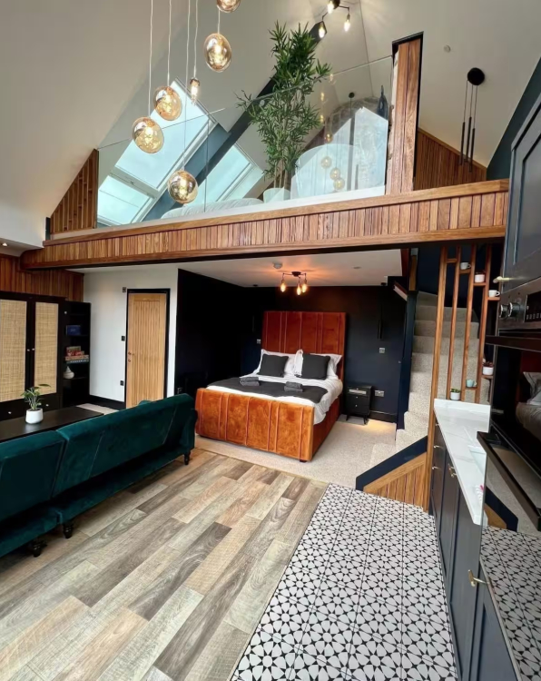 Interior view of a luxury barn conversion with a mezzanine level, featuring a large bed, a green sofa, and patterned flooring.