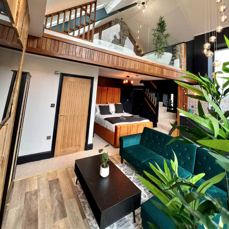 Interior view of a luxury barn conversion with a mezzanine level, a large bed, and a teal sofa.