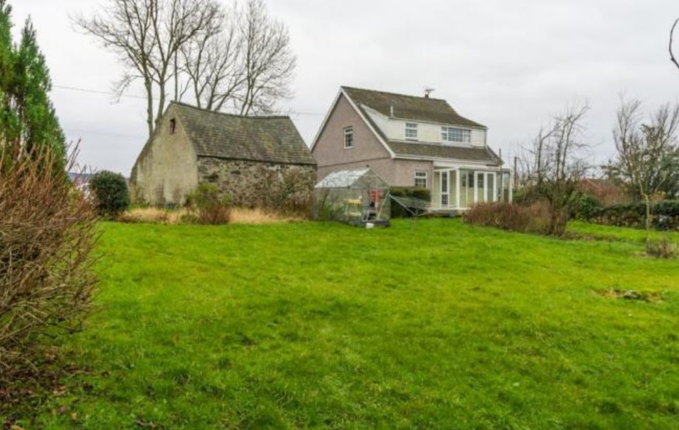 Rear view of a stone barn and renovated house in a grassy yard.
