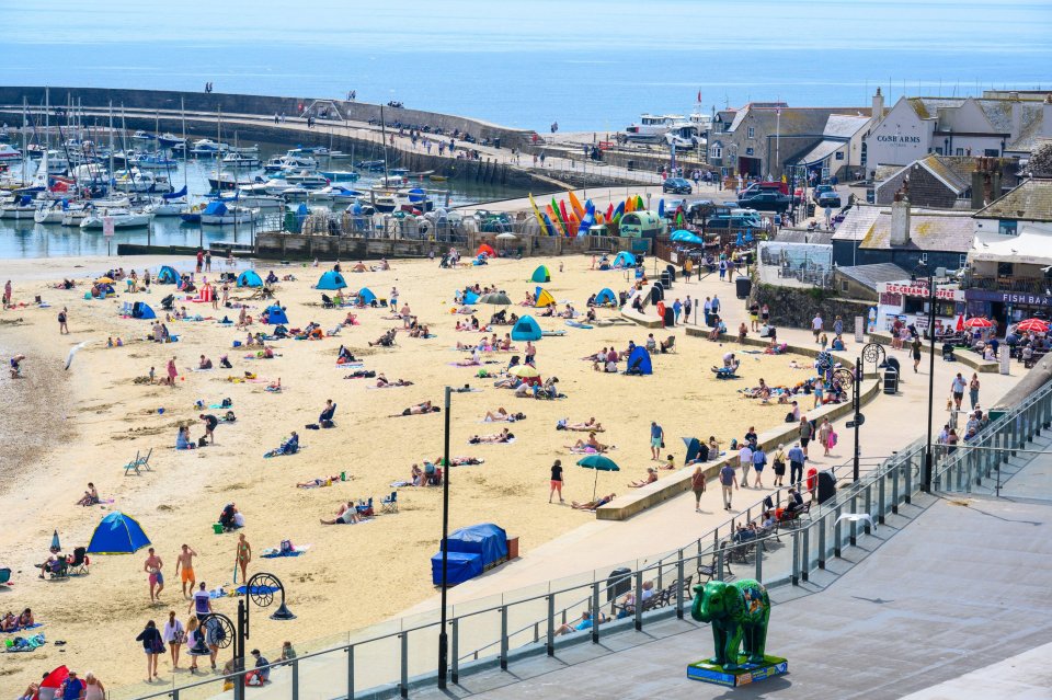 Crowded beach in Lyme Regis, Dorset with many people sunbathing and relaxing.