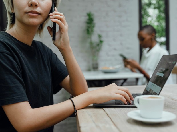 Woman using laptop and phone in cafe.