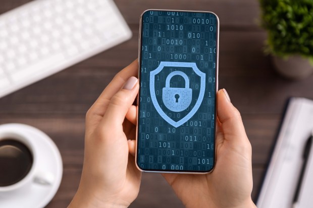 Woman holding smartphone displaying a padlock icon inside a shield on a binary code background.