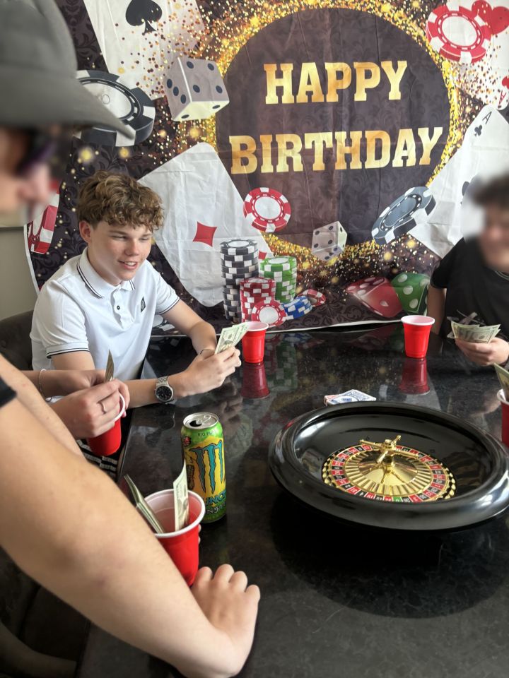 Teenagers playing a casino-themed birthday game with fake money and a roulette wheel.