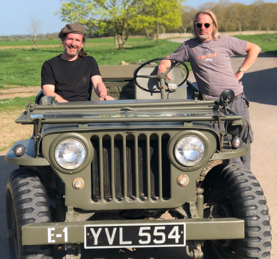 Two men standing by a vintage military jeep.