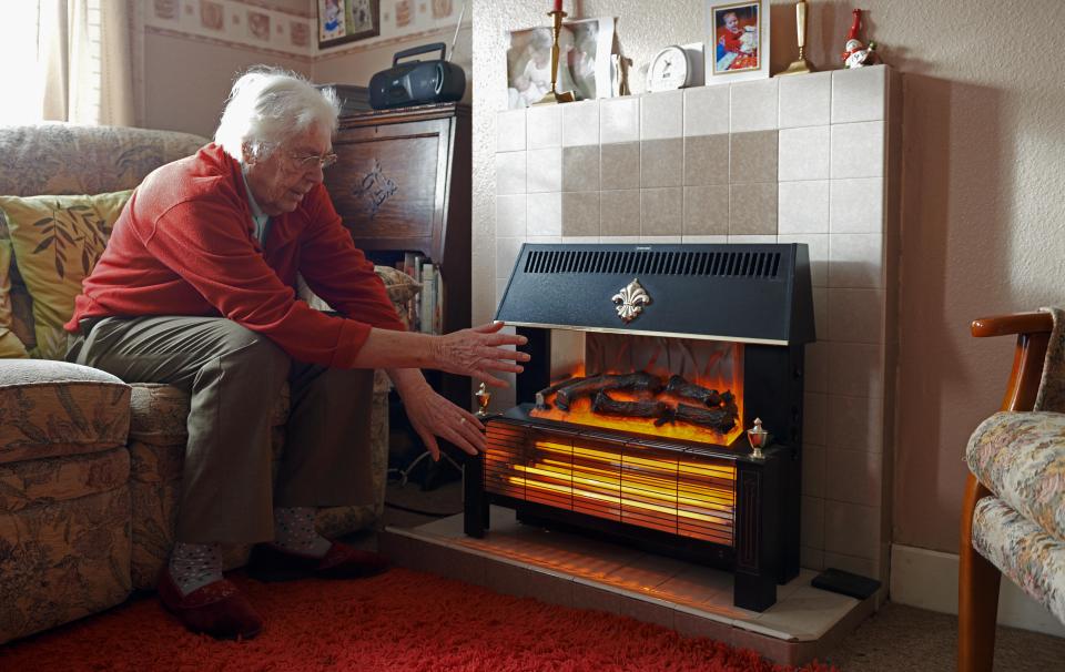 Elderly woman warming herself by an electric fire.