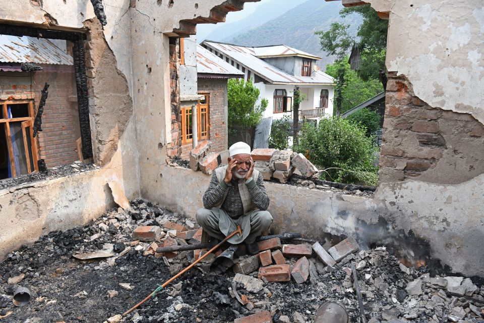 Elderly man sits amid the rubble of a destroyed house.