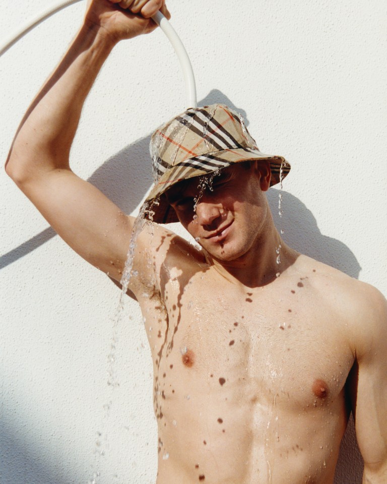Man in a Burberry bucket hat showering outdoors.