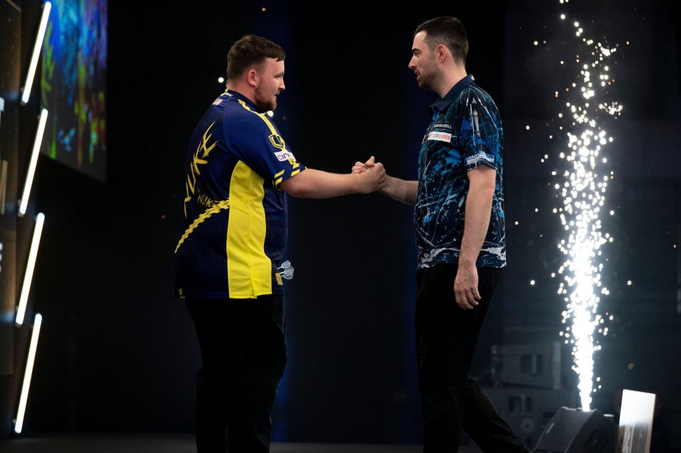 Luke Littler and Luke Humphries shaking hands at a darts competition.