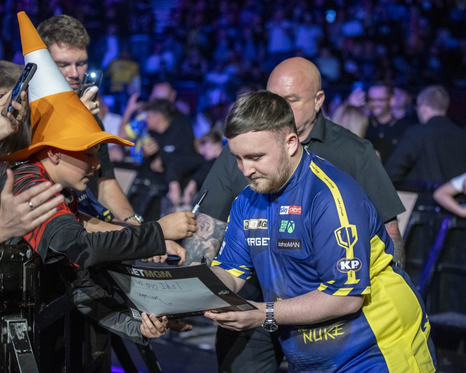 Luke Littler signing an autograph for a fan.