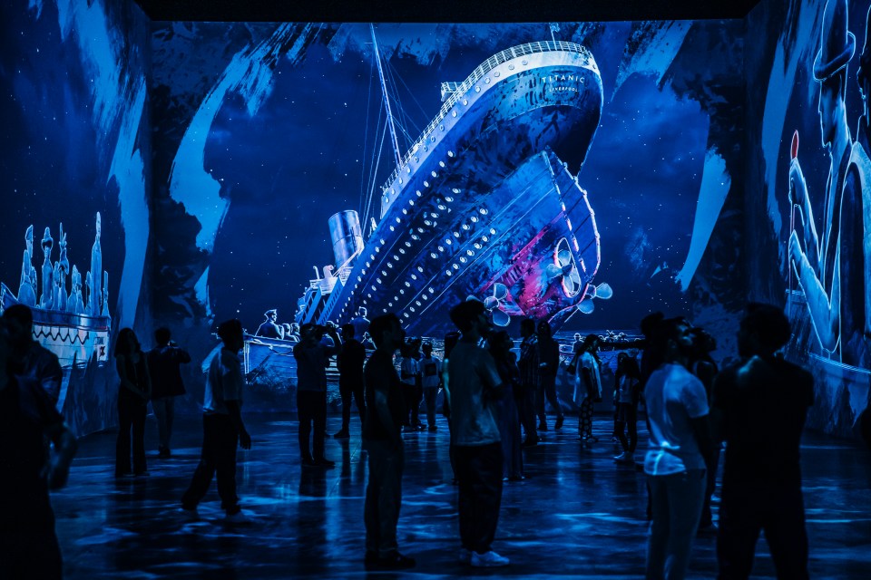 People viewing a large-scale projection of the Titanic sinking.