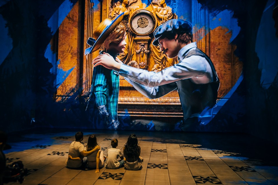 A family watches a large projection of a man and child at a Titanic exhibition.