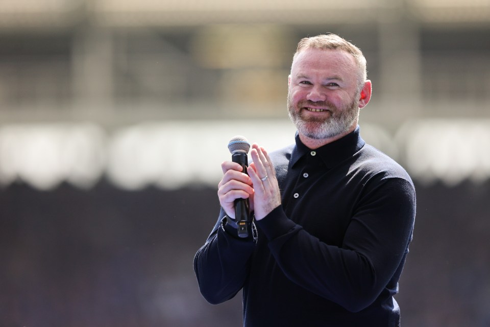Wayne Rooney speaking into a microphone and applauding.