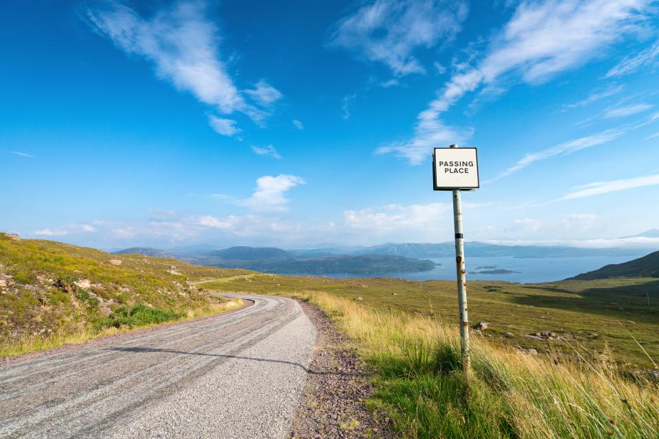 Remote highway with a "Passing Place" sign and scenic mountain views.