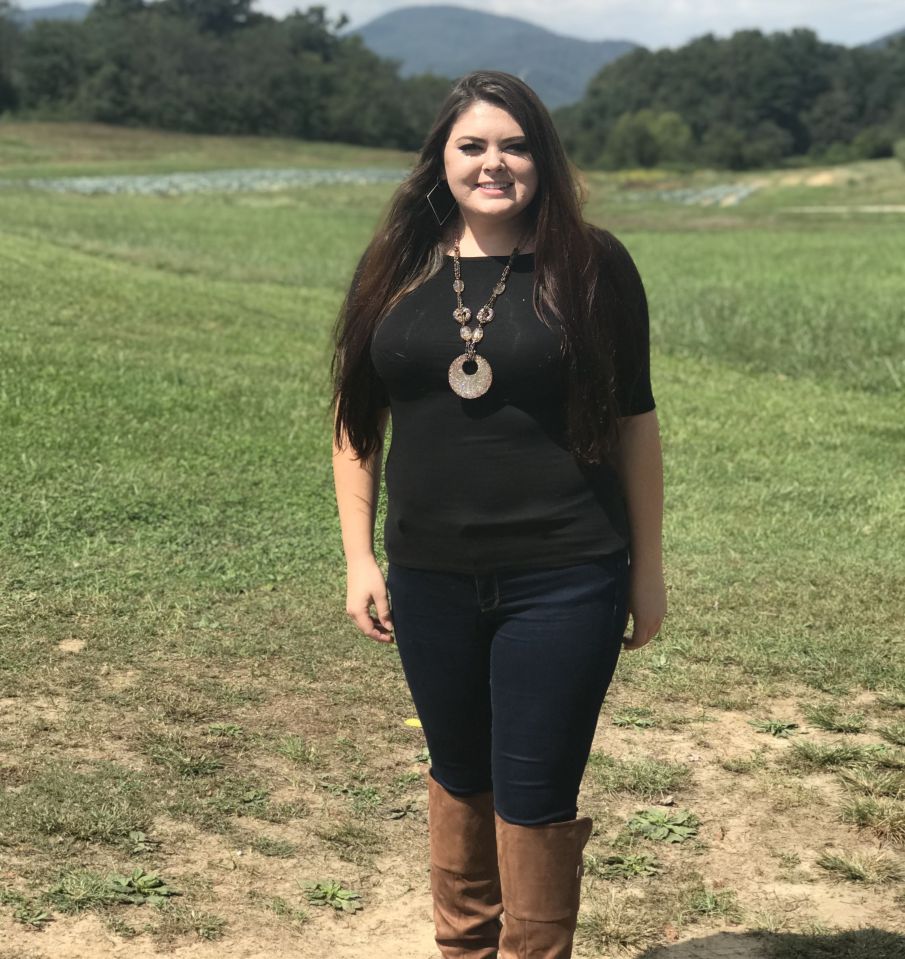 Woman in black top and jeans standing in a field.
