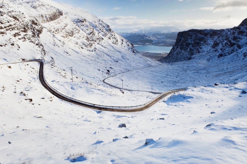 Snow-covered mountain road winding through a valley.